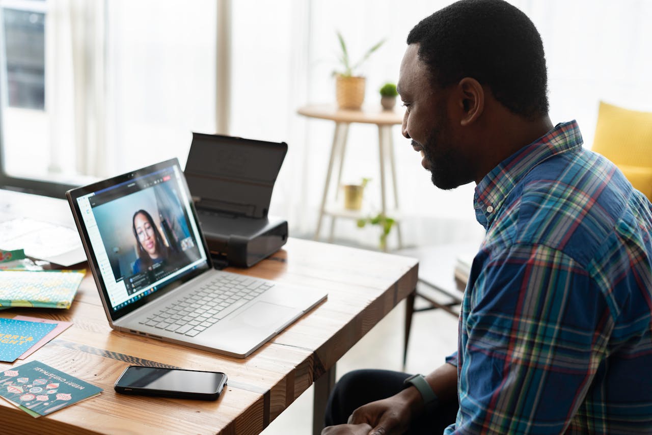 Man engaged in a video call with a colleague at a wooden desk in a modern office setting.